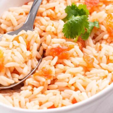 A bowl of Mexican rice with tomatoes and a sprig of cilantro, served with a spoon.