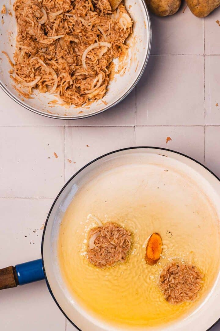 Two pans: one with seasoned shredded mix, the other frying patties and a turmeric piece in oil on a tiled surface.
