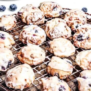 Iced blueberry cookies cooling on a wire rack, with some fresh blueberries in the background.