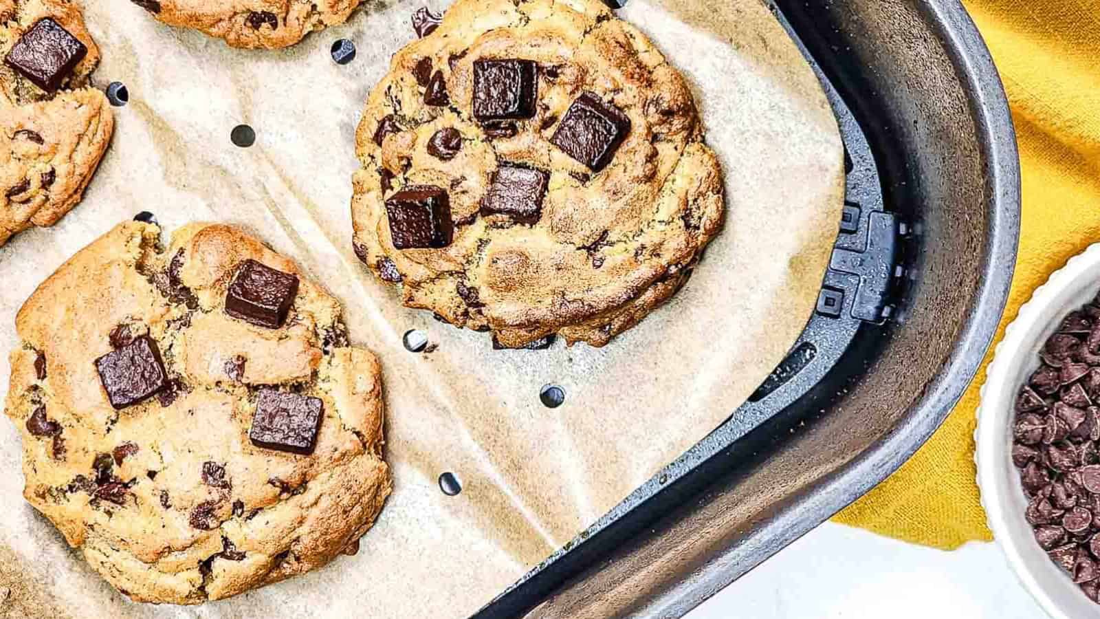 Four chocolate chunk cookies on parchment paper inside an air fryer basket.