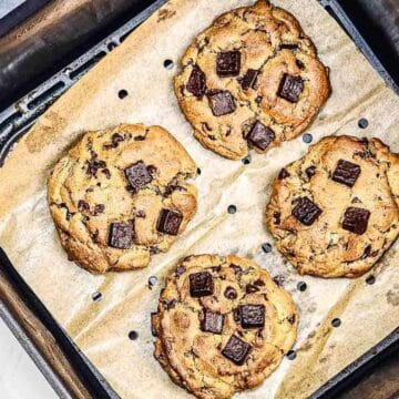 Four chocolate chunk cookies on parchment paper inside an air fryer basket.