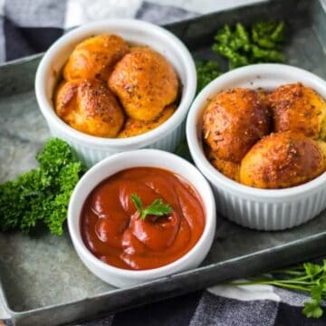 Three ramekins with roasted baby potatoes and a bowl of red dipping sauce on a tray, garnished with parsley.