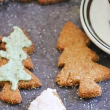 Christmas tree-shaped cookies with icing next to a cup of coffee on a dark surface.
