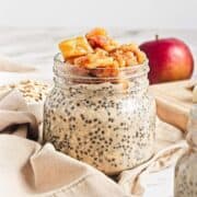 A jar of chia seed pudding topped with caramelized apples, with oats and an apple in the background.