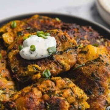 A plate of golden-brown fritters topped with creamy dip and chopped green onions, with more dip in the background.