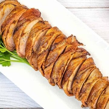 Sliced roasted pork tenderloin on a white platter, garnished with parsley, next to fresh tomatoes.