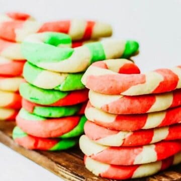 Stacks of red, green, and white striped candy cane-shaped cookies on a wooden board.