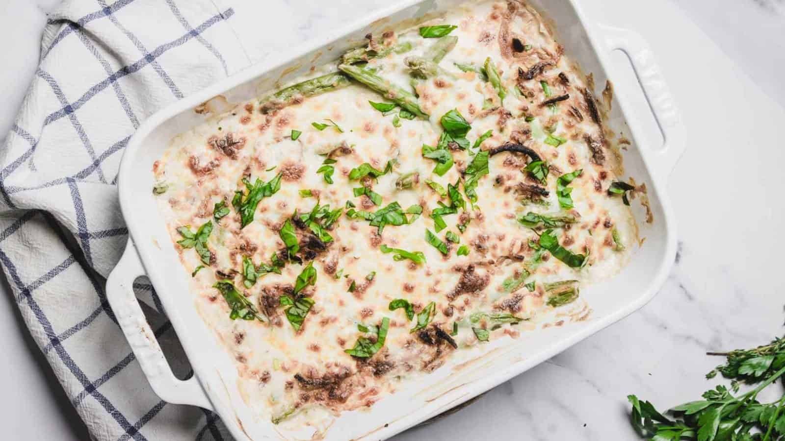 A cheesy green bean casserole being served from a white baking dish with a spoon.