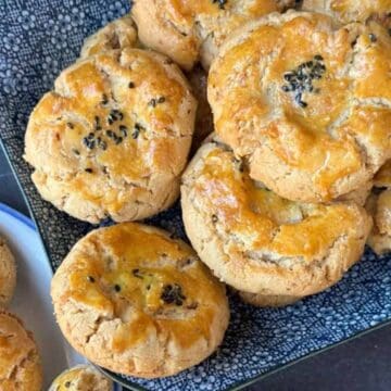 A plate of golden brown cookies topped with black sesame seeds, arranged on a dark patterned dish.