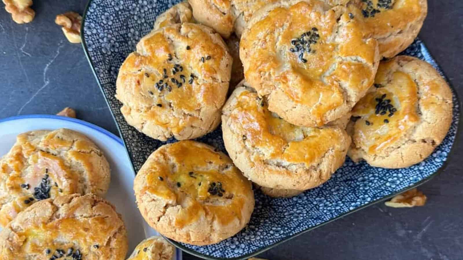 A plate of golden brown cookies topped with black sesame seeds on a dark, patterned tray.