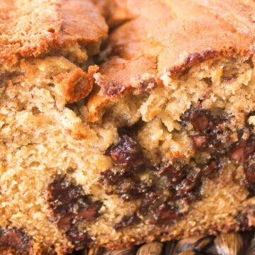A close-up of a sliced loaf of banana bread with visible chocolate chips on a woven mat.