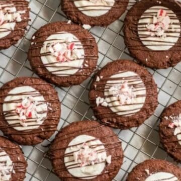Chocolate cookies with white icing, chocolate drizzle, and crushed peppermint on a cooling rack.