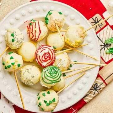 A plate of decorated holiday cake pops on sticks, with red, green, and white frosting and sprinkles.