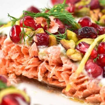 Close-up of cooked salmon topped with pomegranate seeds, pistachios, dill, and lemon zest.
