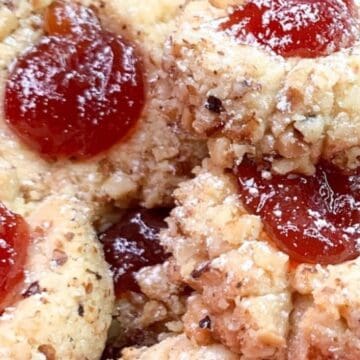 Close-up of thumbprint cookies with nuts and red jam filling, dusted with powdered sugar.