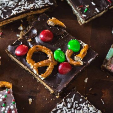 Chocolate bark topped with pretzels, red and green candies, and holiday-themed sprinkles on a wooden surface.
