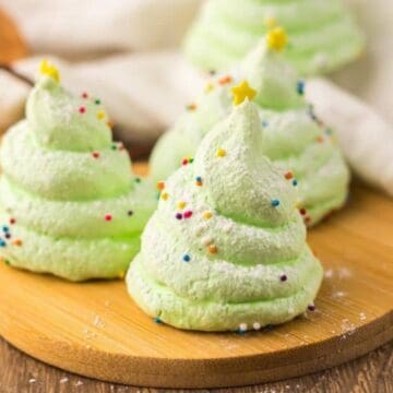 Green Christmas tree-shaped meringues with sprinkles and star toppers on a wooden board.