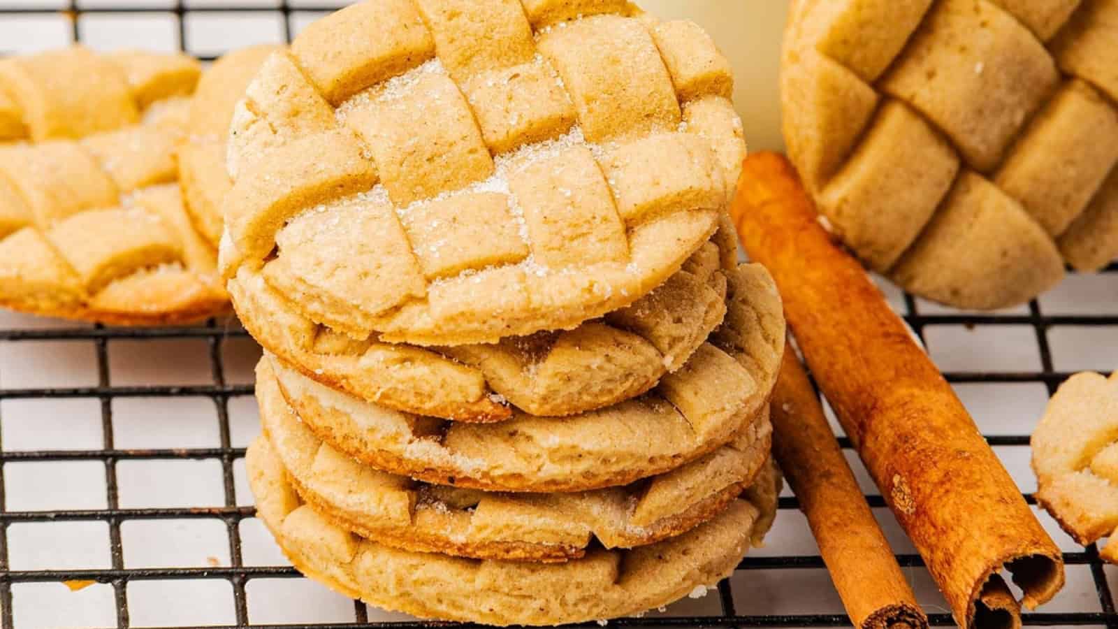 Stacked lattice-patterned cookies beside cinnamon sticks on a cooling rack.