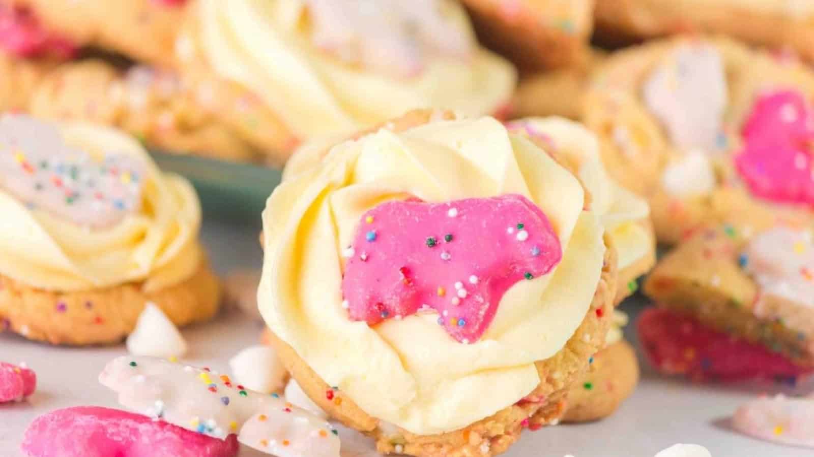 Cookies topped with white and pink animal-shaped frosted cookies and sprinkles, with a creamy yellow frosting layer underneath.