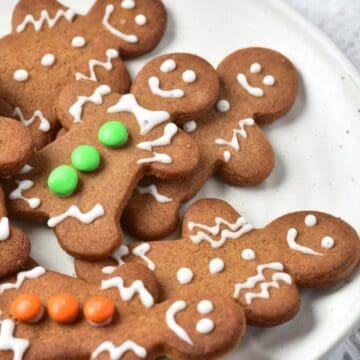 A plate of gingerbread cookies shaped like people, decorated with white icing and colorful candy buttons.