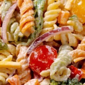 Colorful rotini pasta salad with cherry tomatoes, red onion, vegetables, and creamy dressing.