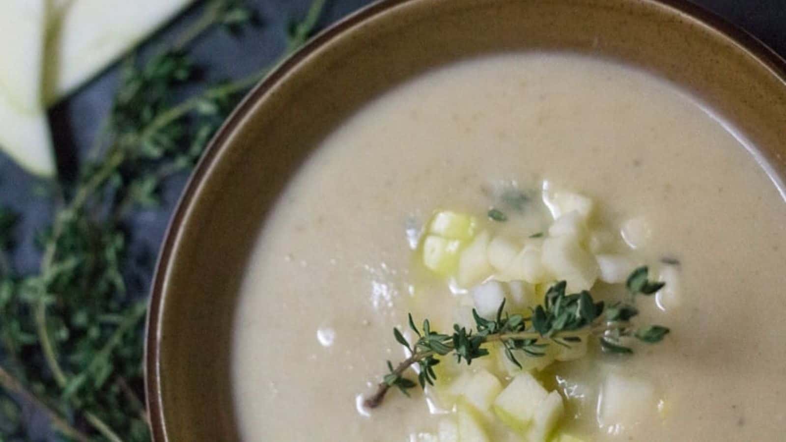 A bowl of soup with apples and sprigs of thyme.
