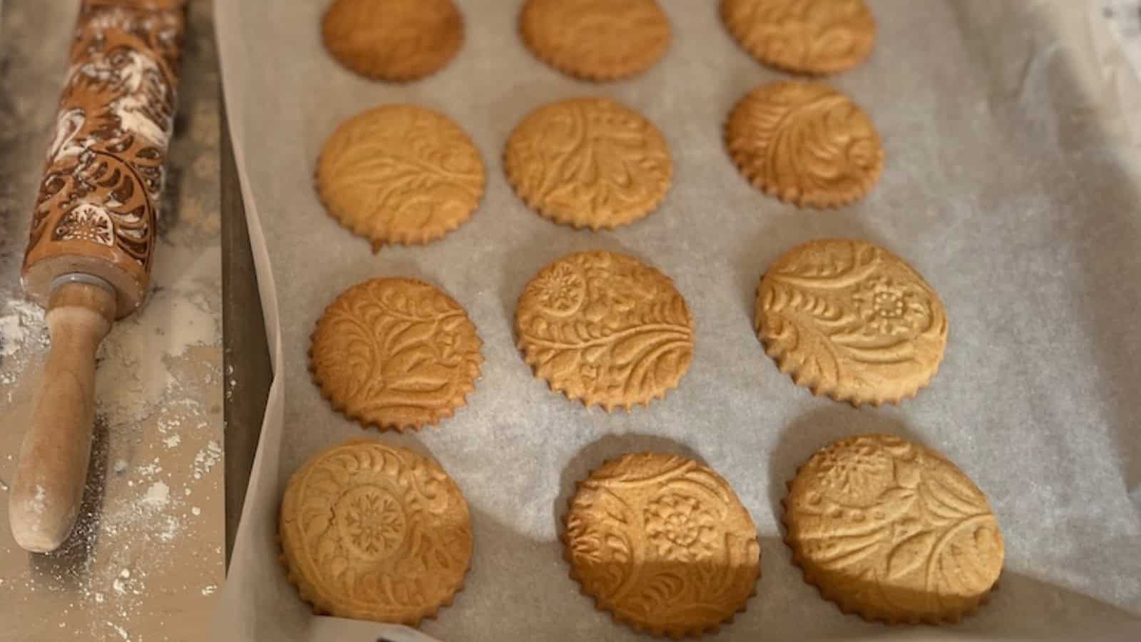 Eight embossed round cookies on a parchment-lined baking sheet. The cookies feature intricate floral and leaf patterns.