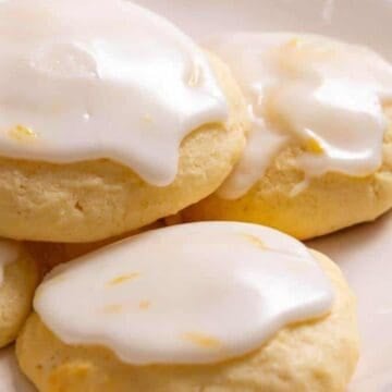Four round cookies topped with white icing, arranged closely together on a white plate.
