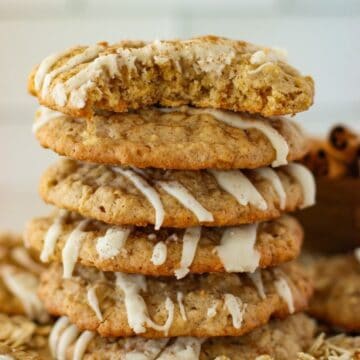 A stack of oatmeal cookies drizzled with icing, with the top cookie partially bitten.