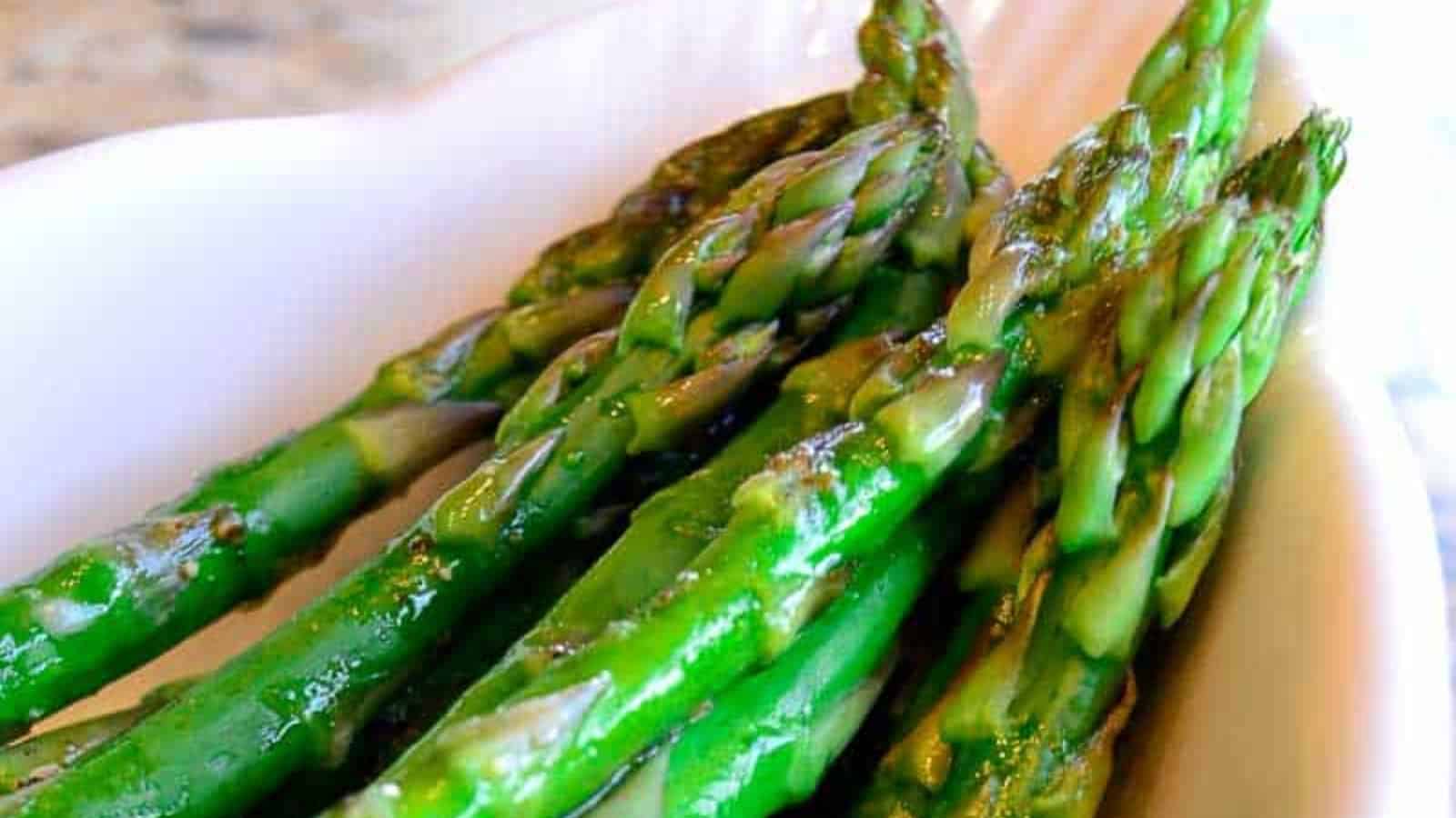 Close-up of cooked asparagus spears glistening with oil, served in a white dish.