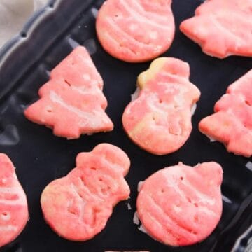 Pink Christmas cookies shaped like trees, snowmen, and ornaments on a black tray.