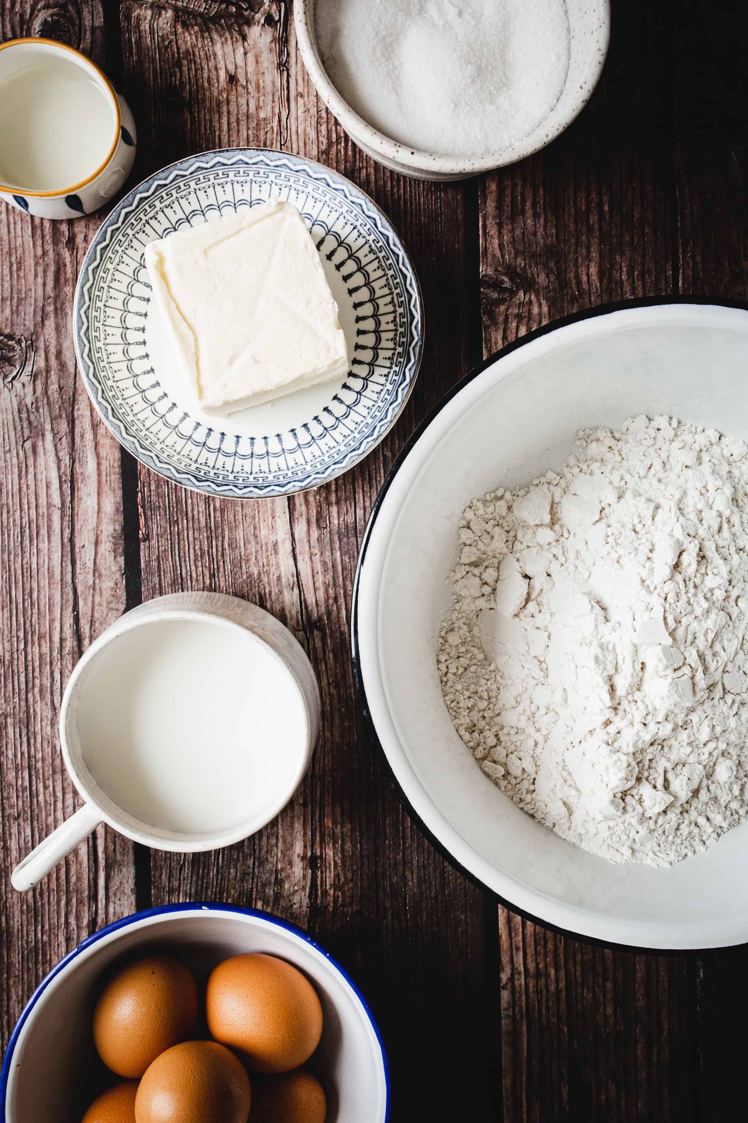 Baking ingredients on a wooden table: flour, eggs, milk, butter, and sugar in bowls and cups&mdash;perfect for creating treats like gluten free ice cream cones.