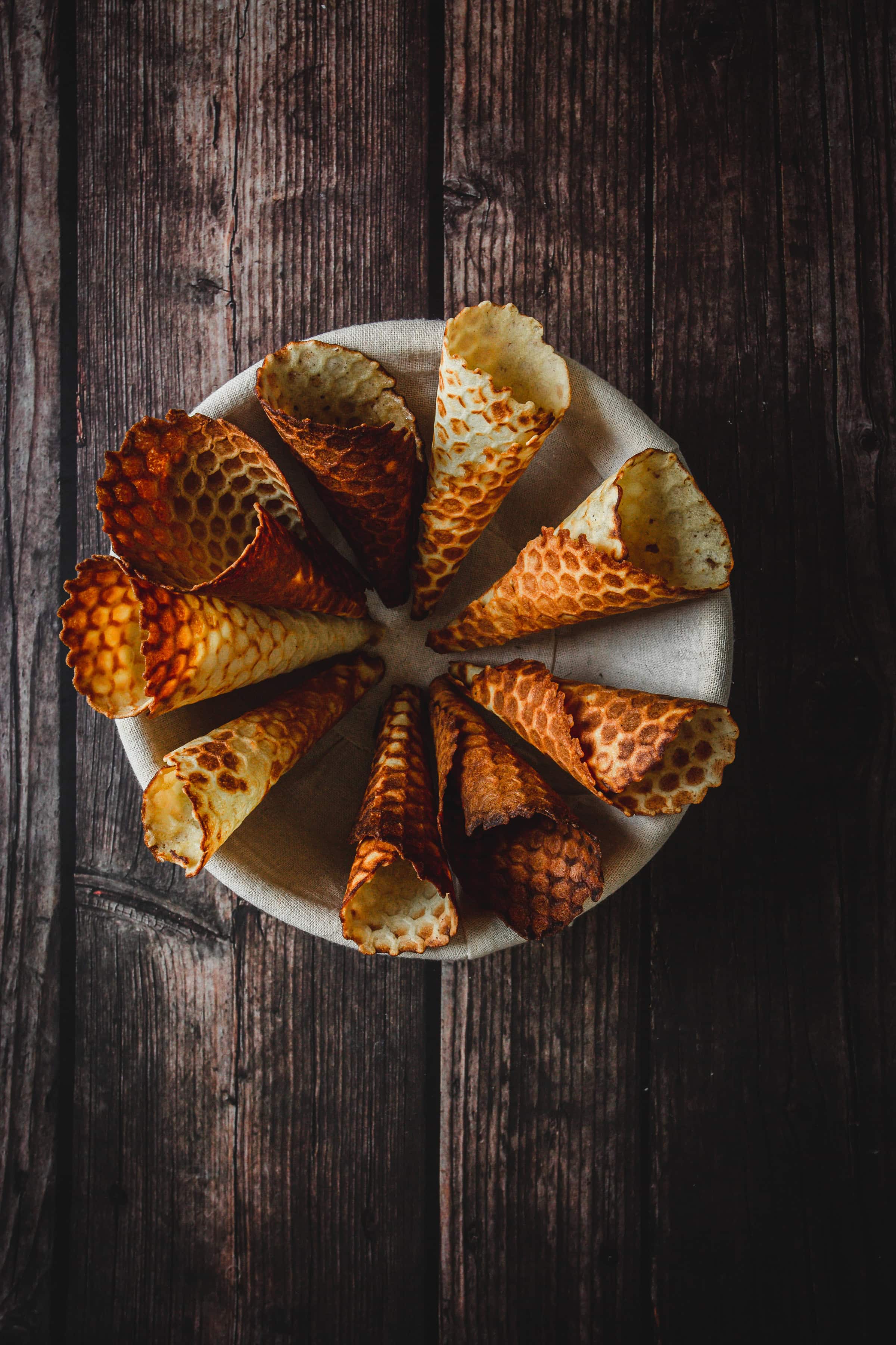 A bowl of empty gluten free ice cream cones arranged in a circle on a rustic wooden surface.