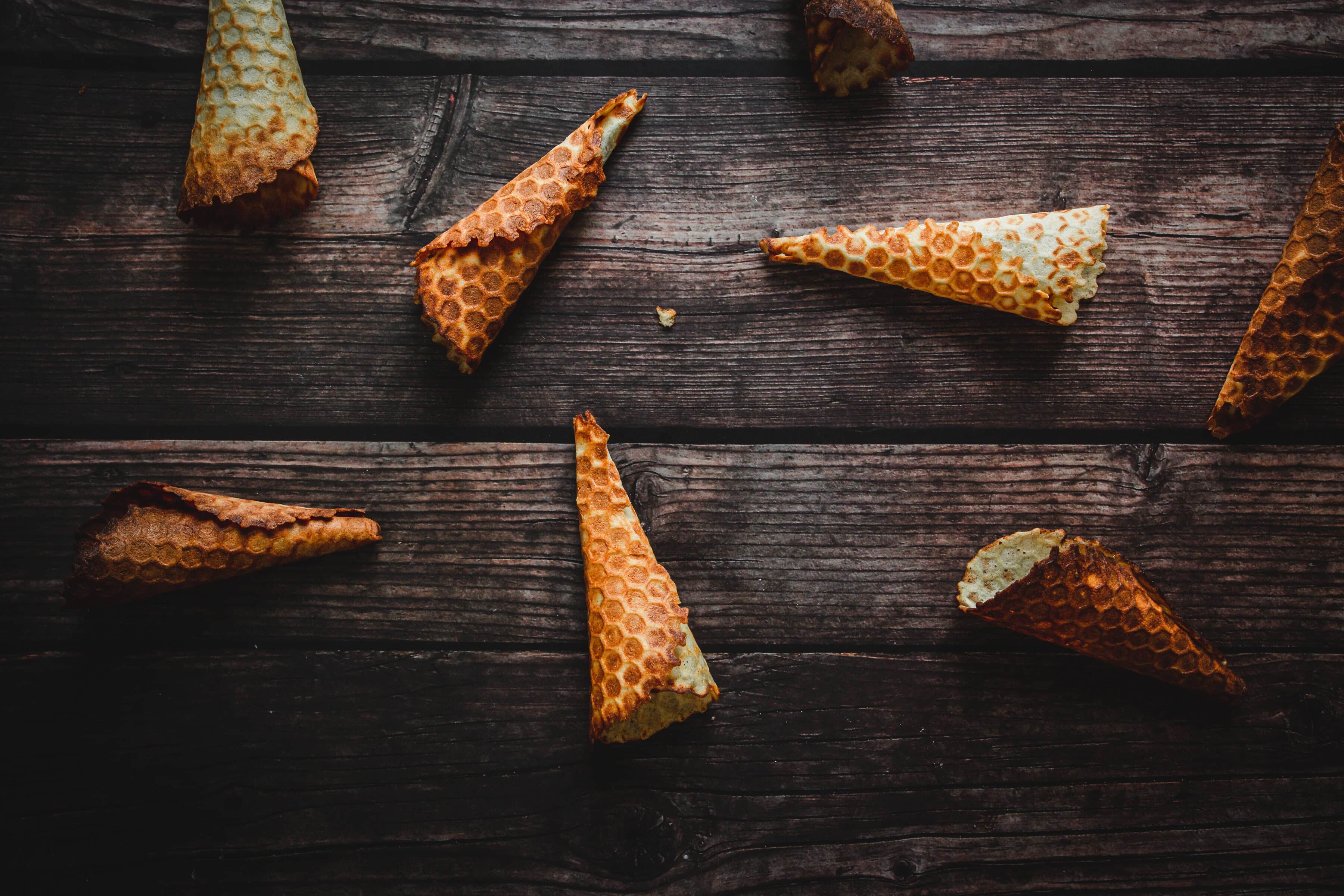 Several empty gluten free ice cream cones are scattered on a dark wooden surface.