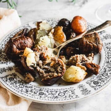 A patterned plate with roasted potatoes and Herbes de Provence Duck Sausage, some pieces cut open with a fork resting on the plate.