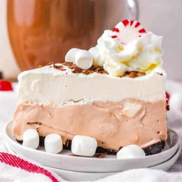 Slice of layered chocolate and vanilla pie topped with whipped cream, marshmallows, and a peppermint candy.
