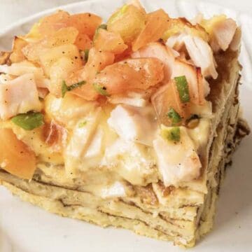 A slice of layered egg casserole topped with chopped tomatoes and herbs on a white plate.