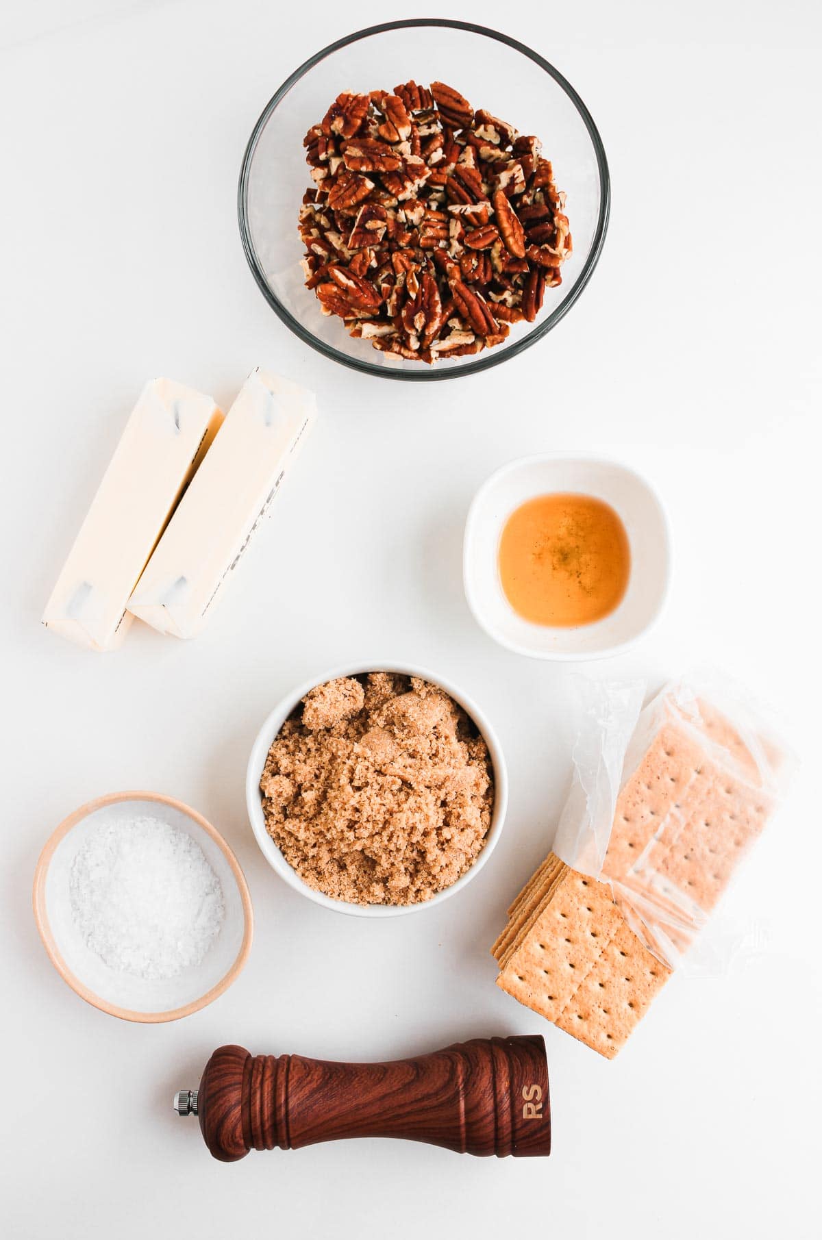 Ingredients for a recipe: pecans, butter, brown sugar, honey, salt, graham crackers, and a pepper grinder.