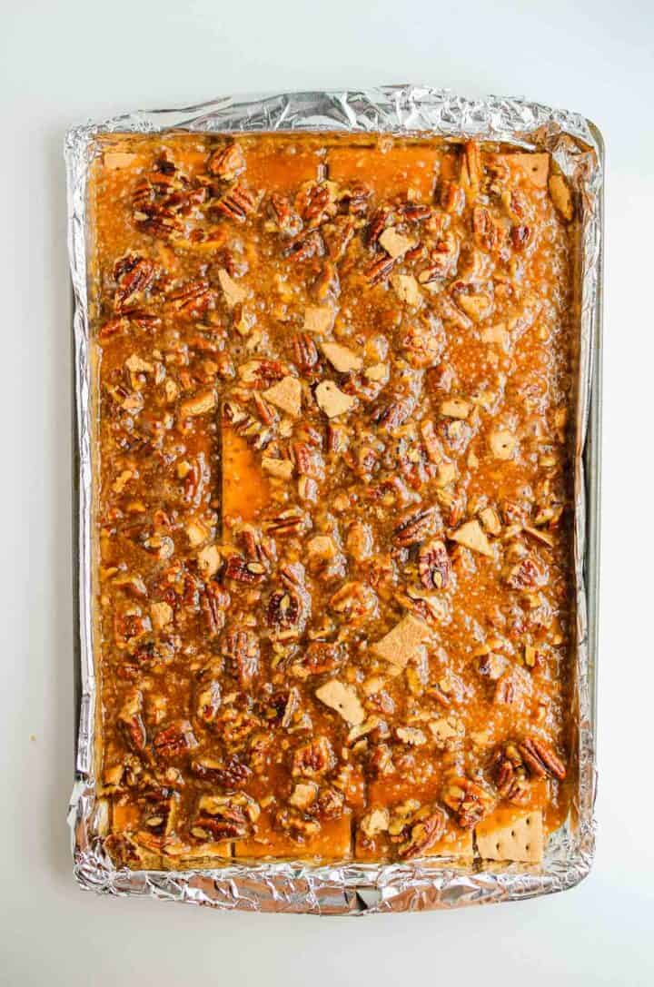 A baking sheet lined with foil holds toffee topped with pecans and crackers.
