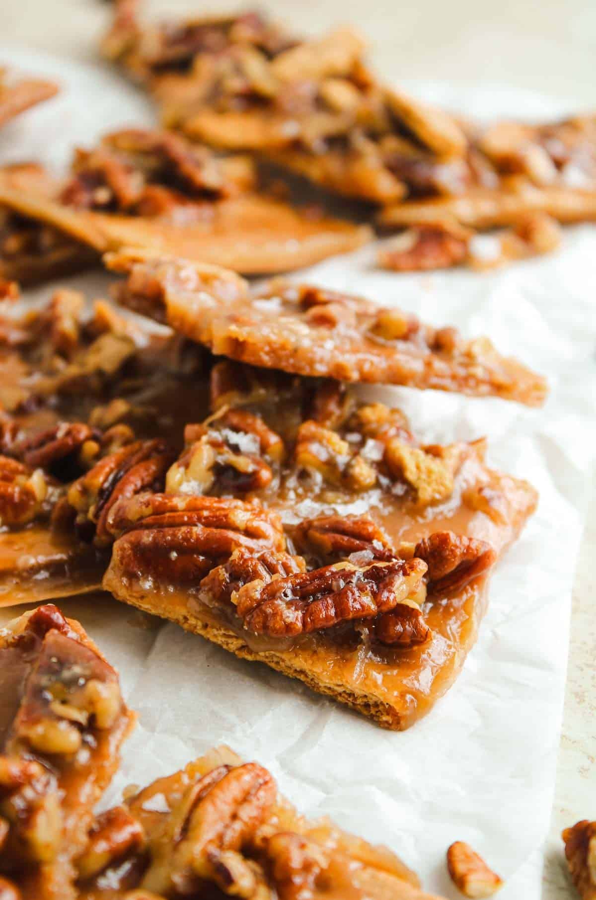 Close-up of pecan praline brittle pieces with caramelized coating on parchment paper.