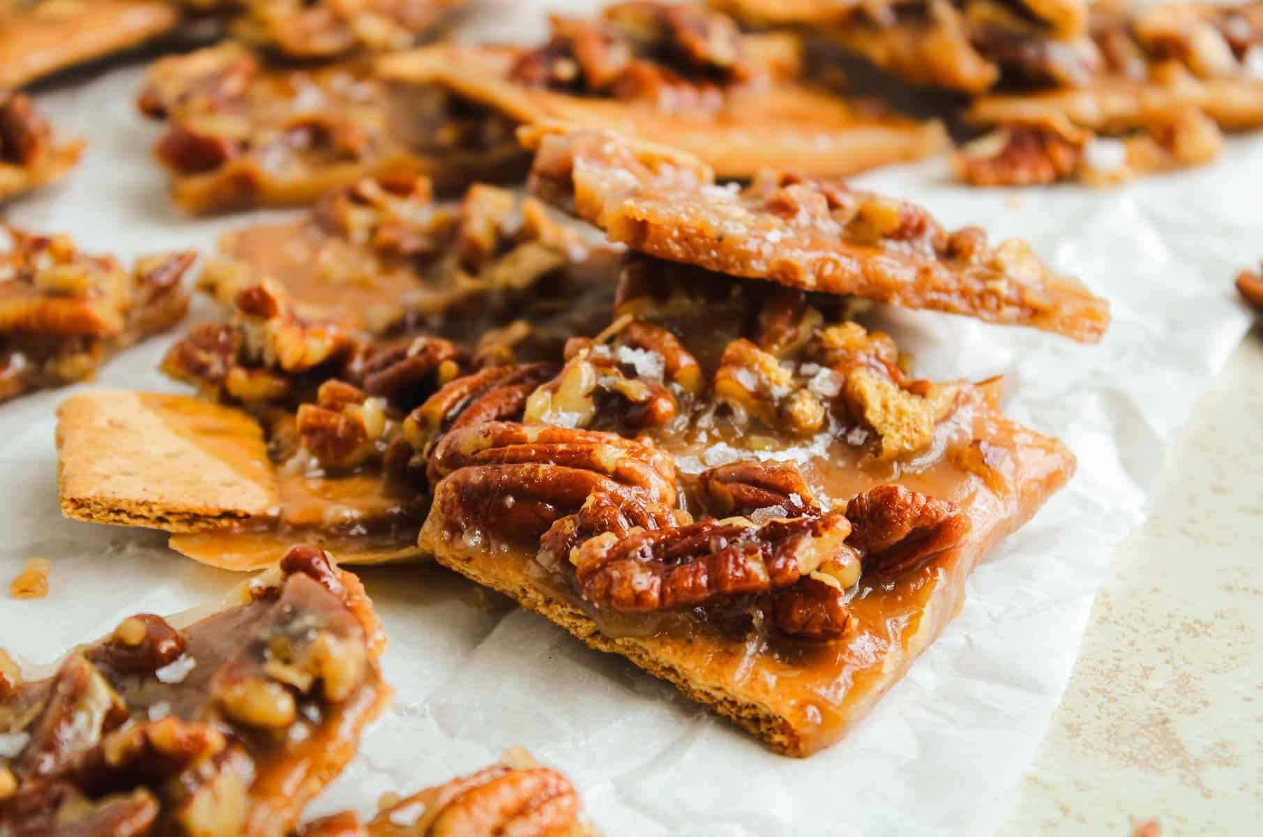 Graham cracker toffee topped with caramelized pecans on parchment paper.