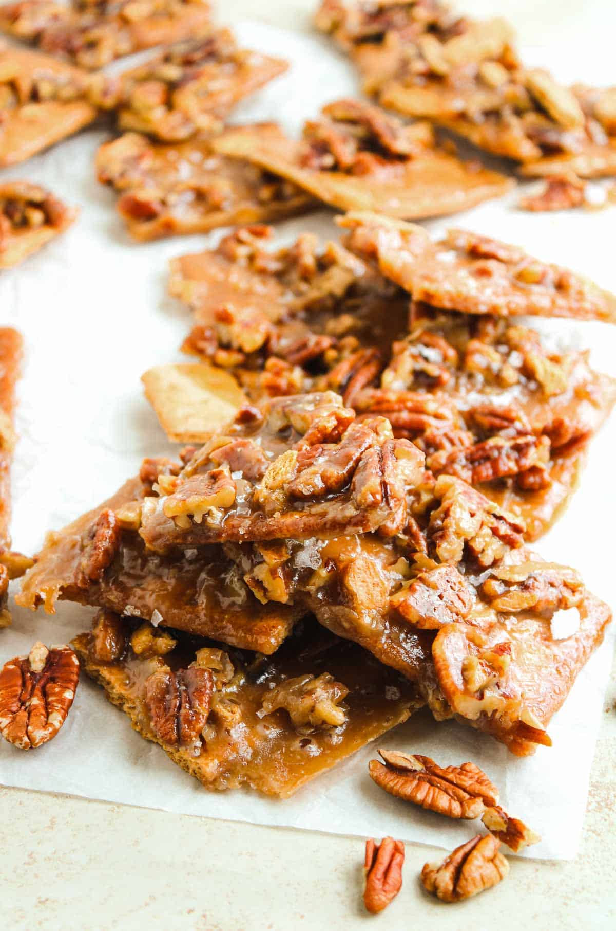 Pieces of homemade pecan brittle stacked on parchment paper, topped with crunchy pecans.