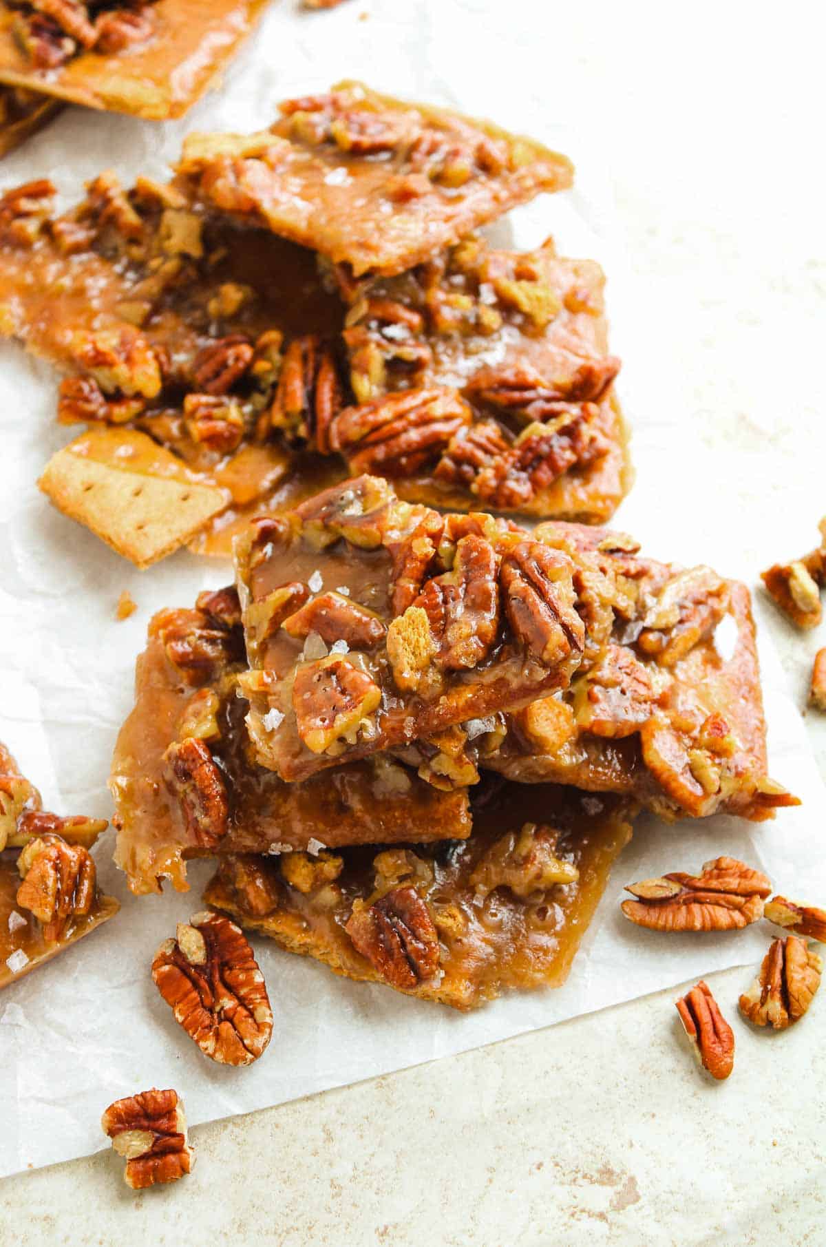 Pecan toffee bark pieces stacked on parchment paper with scattered pecan halves around them.