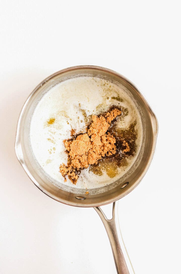 A saucepan with melted butter and a mound of brown sugar on a white background.