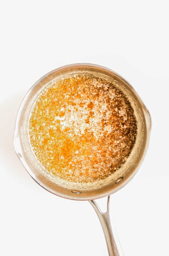 A saucepan filled with melted browned butter on a white background.