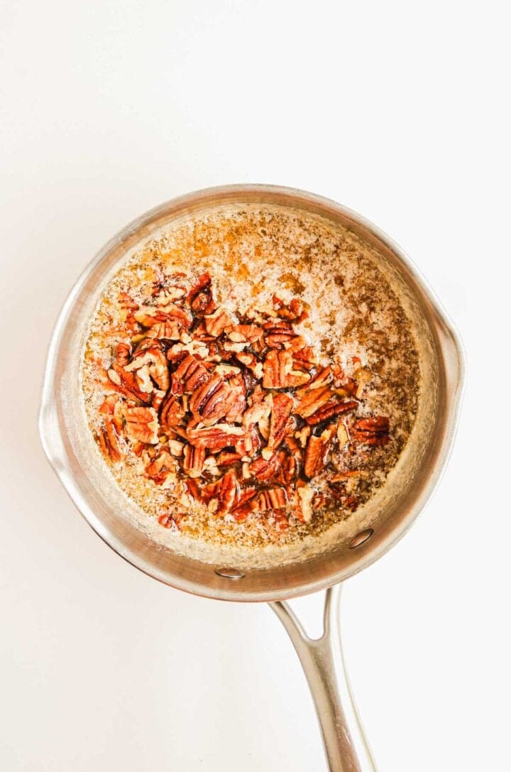 A stainless steel pan with melted butter and chopped pecans on a white background.