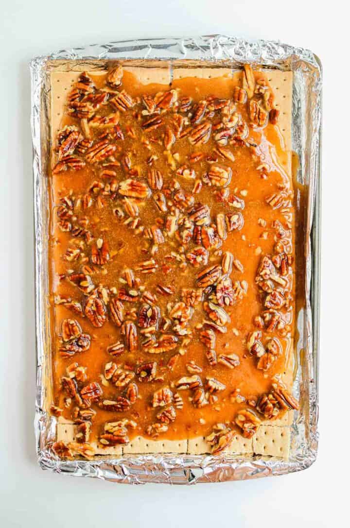 A baking sheet with pecan toffee spread over a layer of graham crackers on foil.