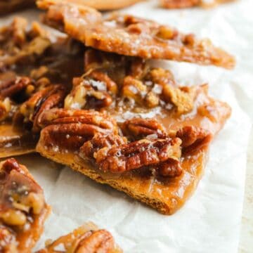Close-up of pieces of pecan brittle on parchment paper, showing caramelized sugar and whole pecans.