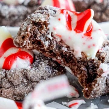Chocolate crinkle cookies topped with red and white striped peppermint kisses, with one cookie broken in half.