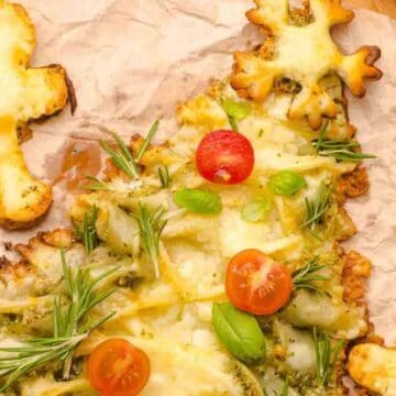 Christmas tree-shaped cheesy bread with cherry tomatoes and herbs, surrounded by star and gingerbread shapes.